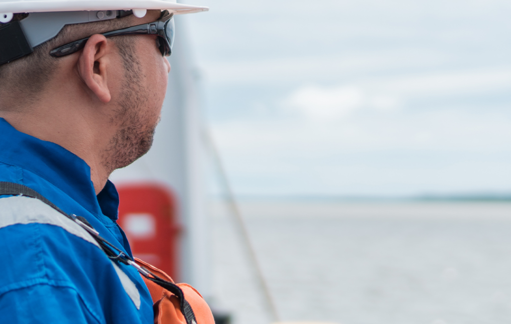 man wearing a life jacket, safety helmet, and sunglasses, looking out over the sea